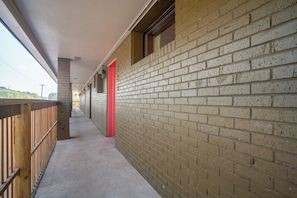 Un pasillo con pared de ladrillo, barandilla de madera y una puerta roja.