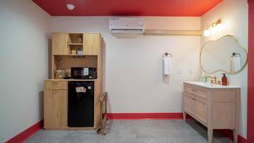 A compact bathroom with a built-in microwave, a refrigerator, a vanity with a mirror, and an air conditioning unit.