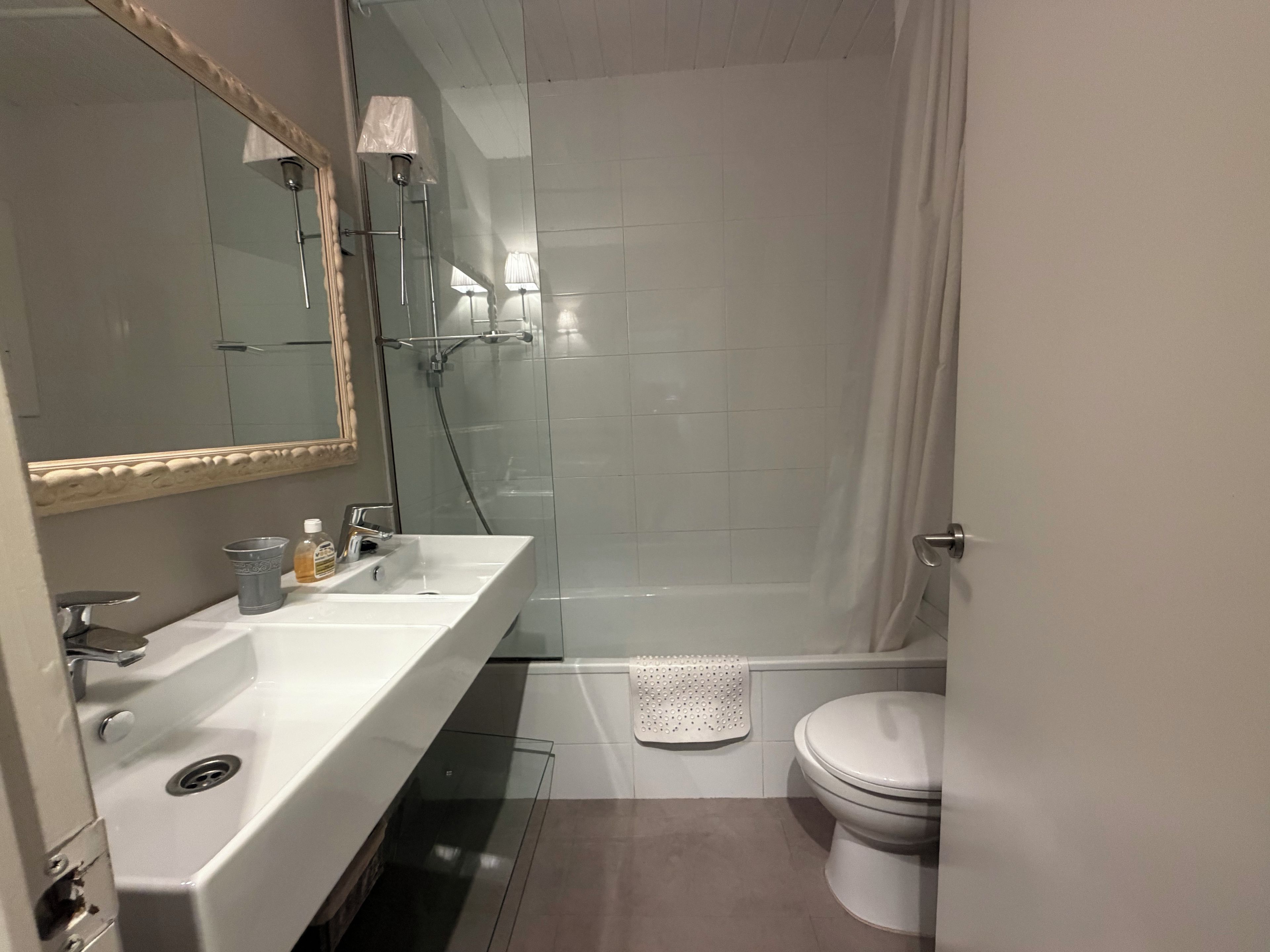 Un baño moderno con lavamanos, espejo, ducha e inodoro blancos.