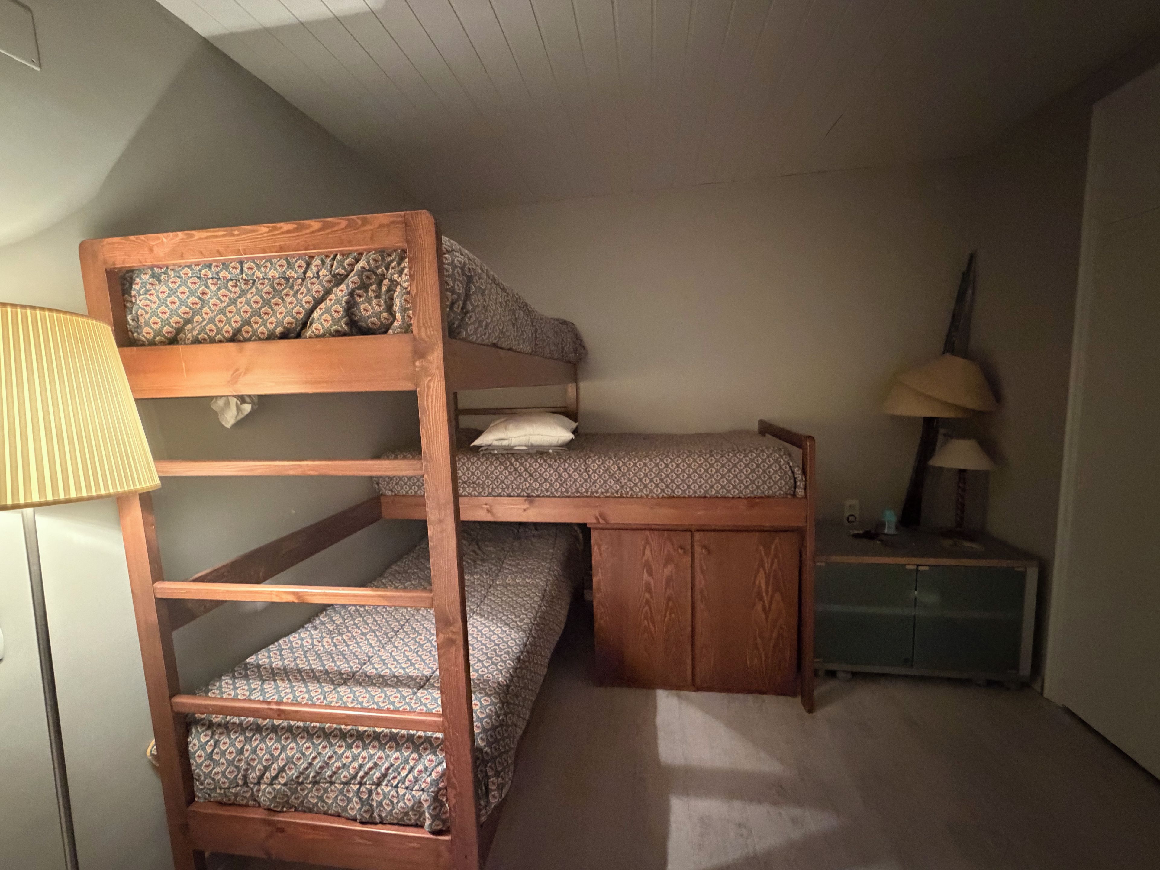 Una cama litera con escritorio y lámpara, un mueble pequeño y una lámpara en una mesita de noche.