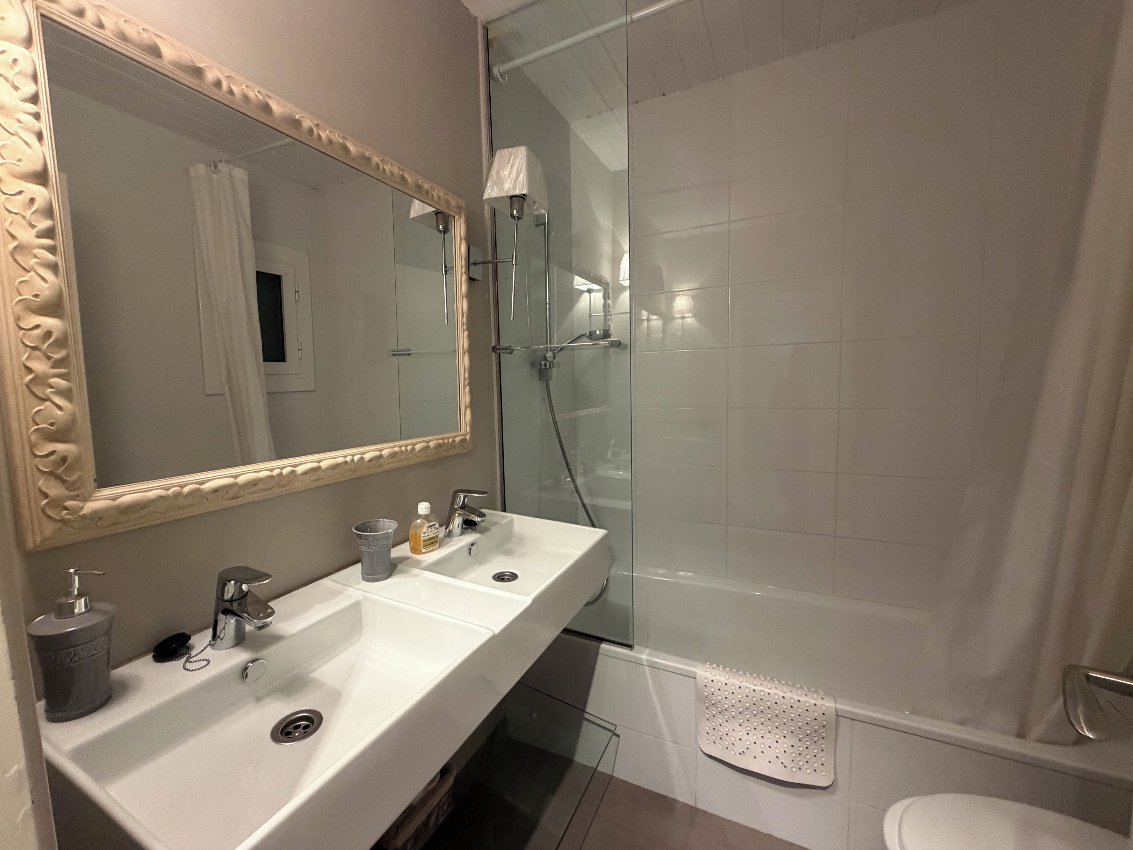 Un baño con un espejo grande, dos lavamanos, una ducha e inodoro.