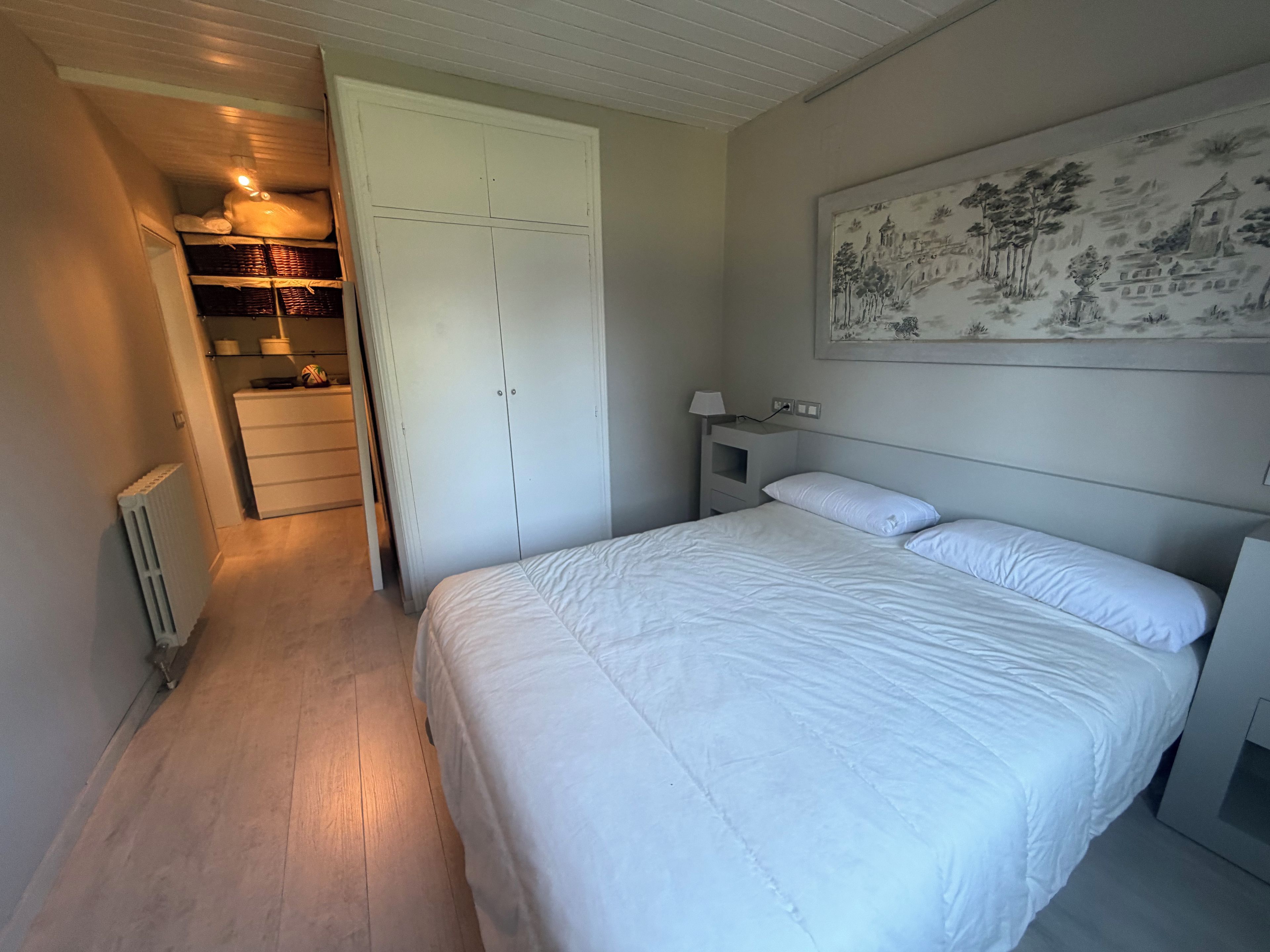 Un dormitorio con cama, mesita de noche, lámpara, radiador y armario.