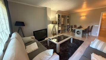 Una sala de estar moderna con un sofá, televisor, mesa de centro y un comedor con sillas y una mesa.