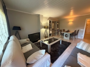 Un salon moderne comprenant un canapé, un téléviseur, une table basse et un coin repas avec des chaises et une table.