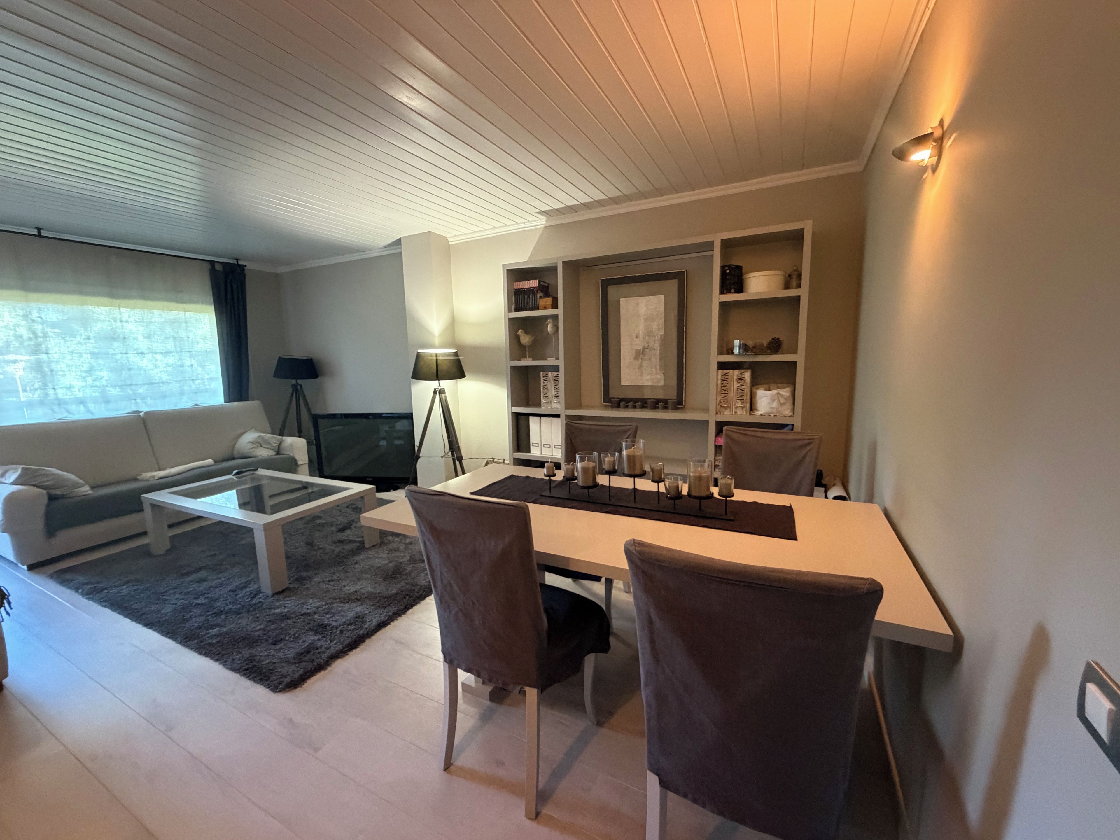 Una sala moderna con sofá, mesa de centro y sillas, un comedor con mesa y sillas, y una estantería con objetos decorativos.