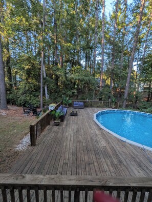 Une terrasse en bois avec une piscine, entourée d’arbres et de verdure.
