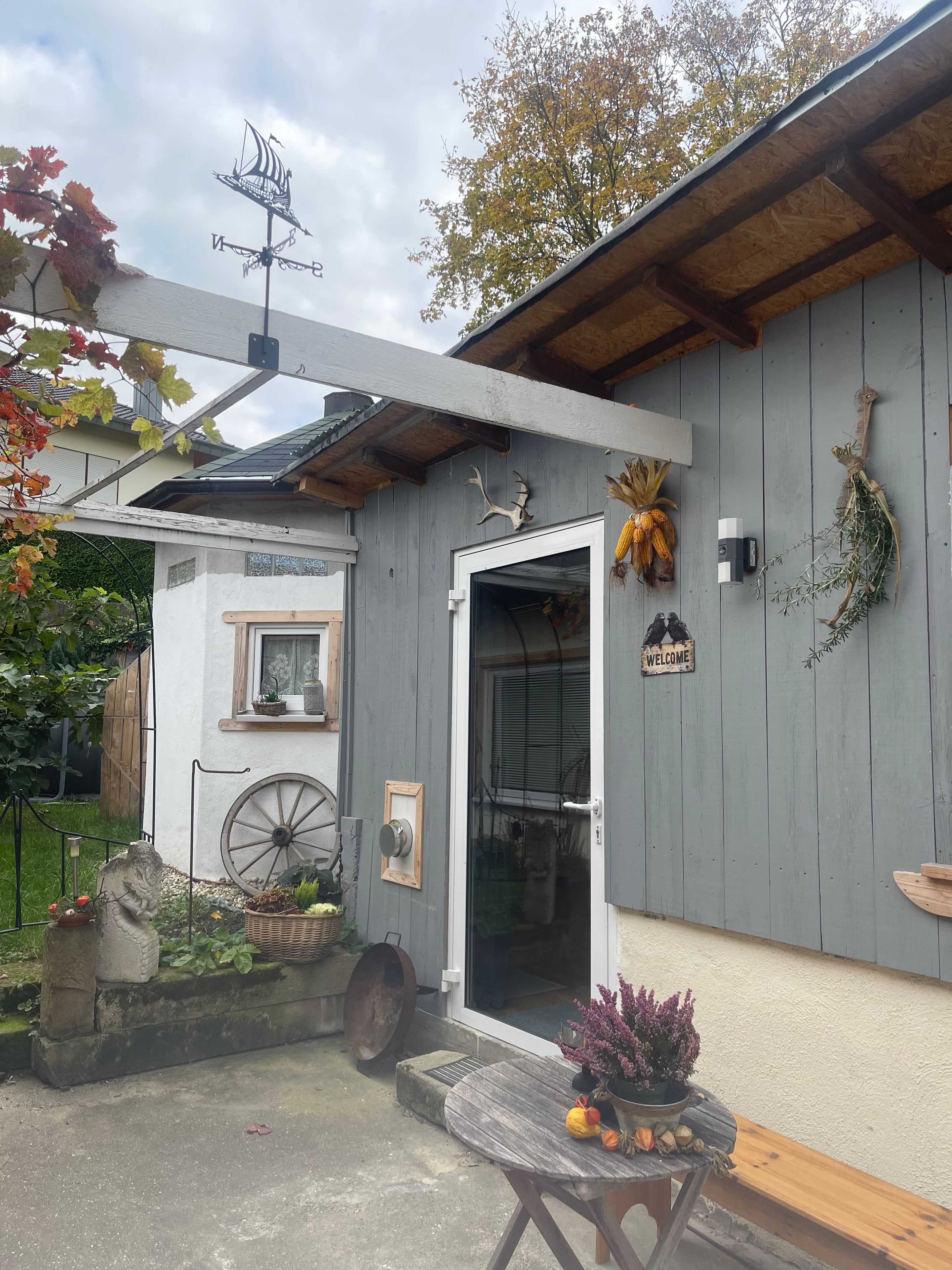 Une cabane rustique, ornée d’une girouette, d’une pancarte de bienvenue et d’une brouette devant l’entrée.
