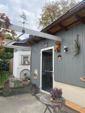 A rustic cabin with a weather vane, a welcome sign, and a wheelbarrow outside.