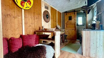 A rustic interior with a wooden ceiling, a round shield decoration, a fur-covered bench, and a wooden dining table.