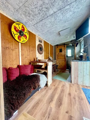A rustic interior with a wooden ceiling, a round shield decoration, a fur-covered bench, and a wooden dining table.