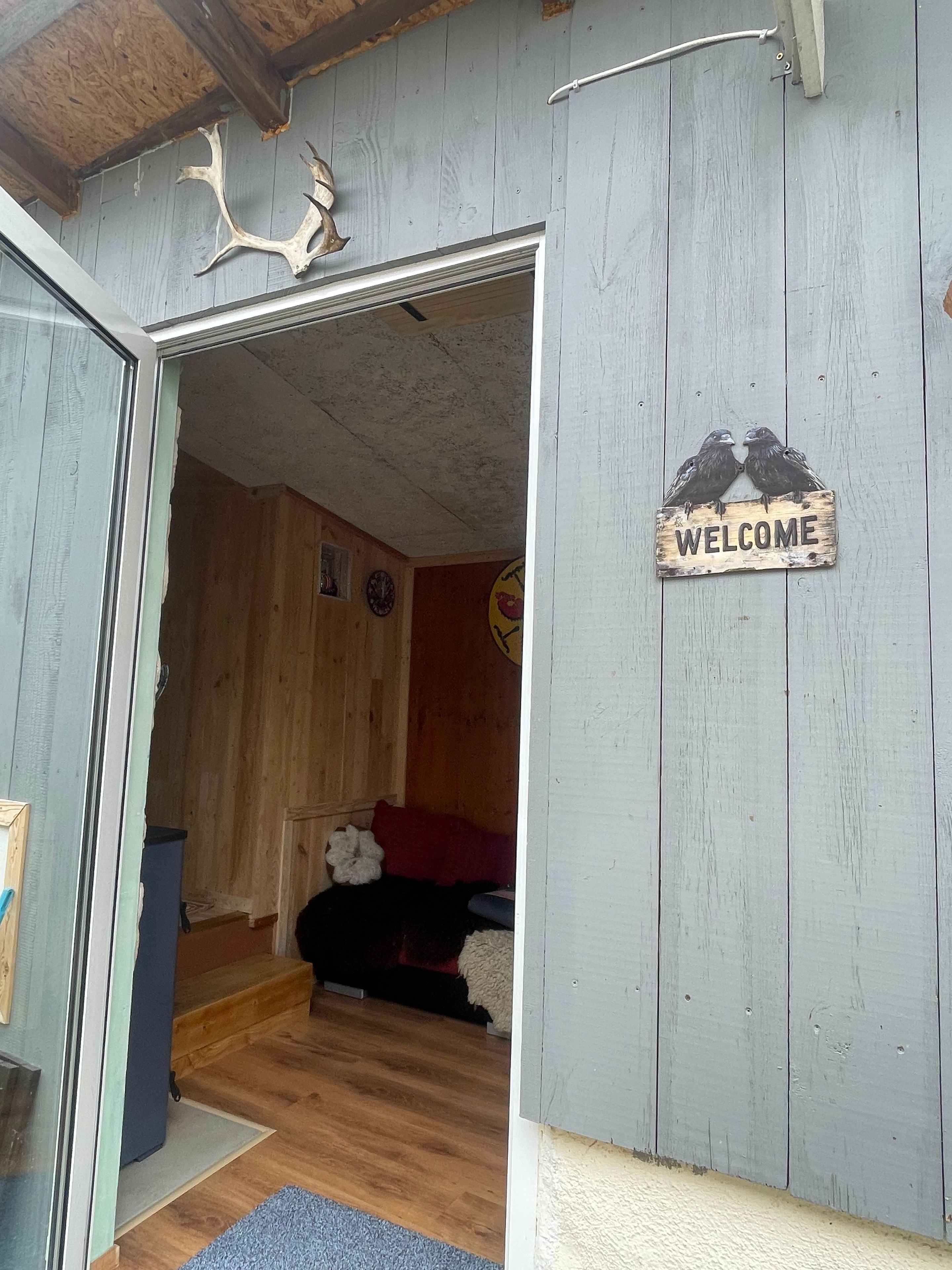 Een houten interieur met een 'WELCOME' bord, een klok en een rustieke inrichting, waaronder gewei.