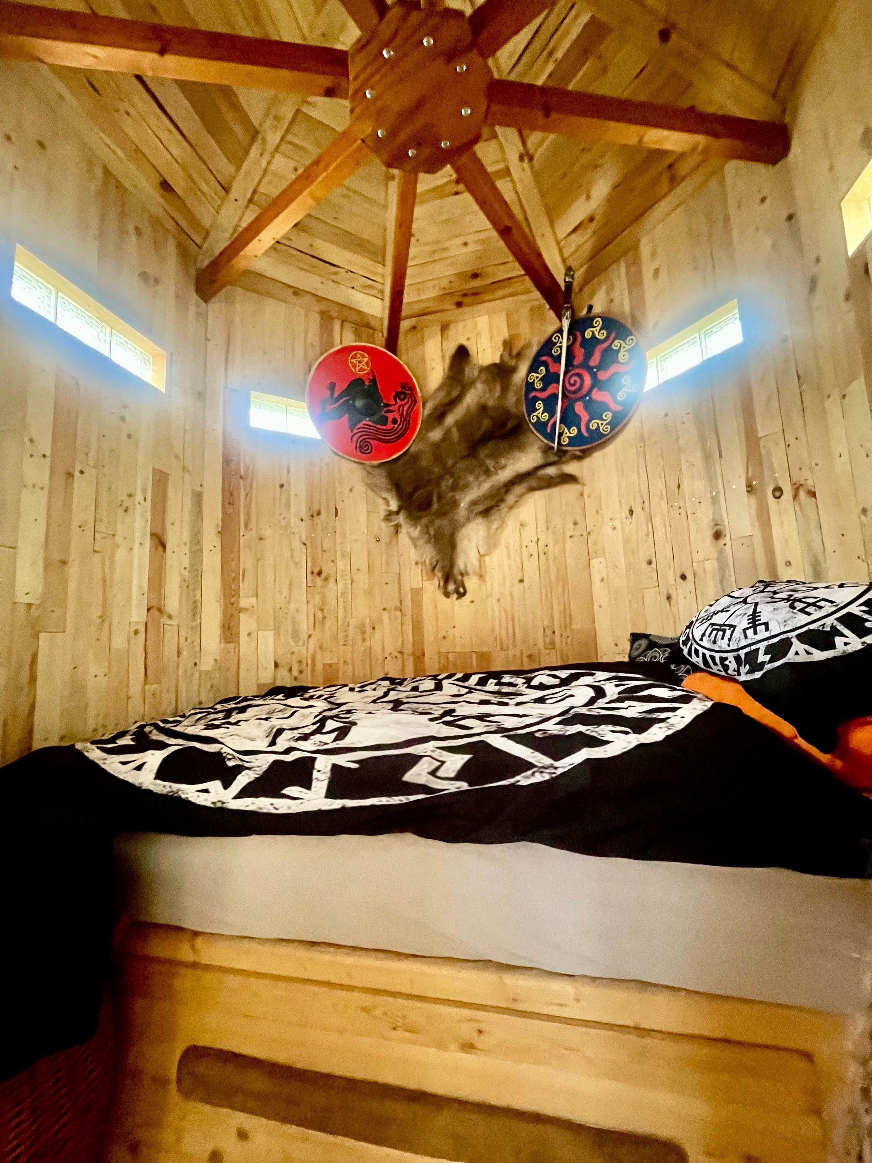 A room with wooden walls, a slanted ceiling, and a bed with a patterned blanket.