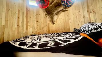 A room with wooden walls, a slanted ceiling, and a bed with a patterned blanket.