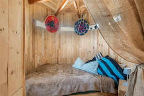 A wooden room with a bed, two decorative shields, and a hanging net.