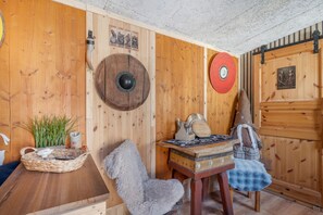 A rustic wooden interior with a round wooden table, a chair, and a decorative shield on the wall.