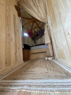 A wooden interior with a sloped ceiling, a bed with a patterned headboard, and a woven rug on the floor.