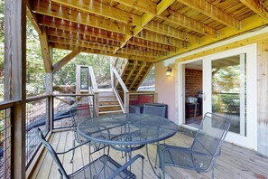 An outdoor patio with a round metal table and chairs, wooden deck, and a covered area with a sloped ceiling. - Mountain House, Mountain Views, Hot Tub, Game Room, Pool Table, Pinball, Decks & BBQ (Otto)