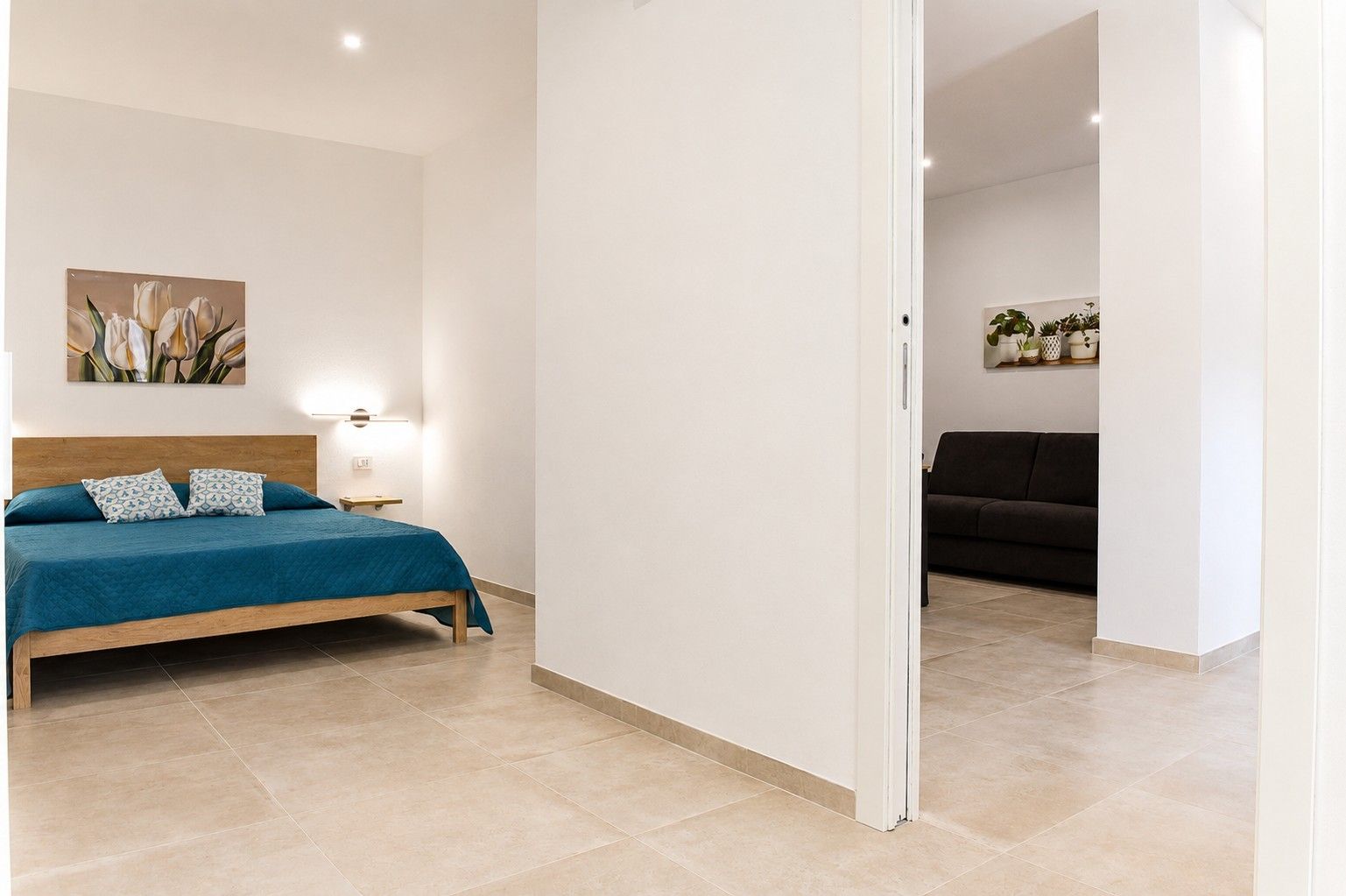 A bedroom with a bed, a bedside table, a wall-mounted lamp, and a painting.