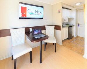 A hotel room with a seating area featuring a laptop on a table, a microwave, and a kitchenette. - Apart Hotel Cambiaso (Providencia)