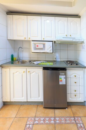 A kitchen with white cabinets, a microwave, a sink, and a refrigerator. - Apart Hotel Cambiaso (Providencia)