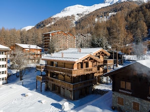 Eine Holzchalet mit mehreren Balkonen, umgeben von schneebedeckten Bäumen und Bergen.