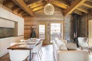 Un intérieur chaleureux et rustique, avec un plafond en bois, des murs en pierre, une cheminée et un coin repas doté de meubles blancs.