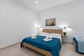 A hotel room with a bed, bedside tables, a wall-mounted painting, and a potted plant. - 'Kero House' Apartment with Wi-Fi and Air Conditioning (Alghero)