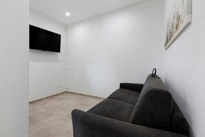 Een woonkamer met een flatscreen televisie aan de muur, een grijze bank en een lijst met een foto.