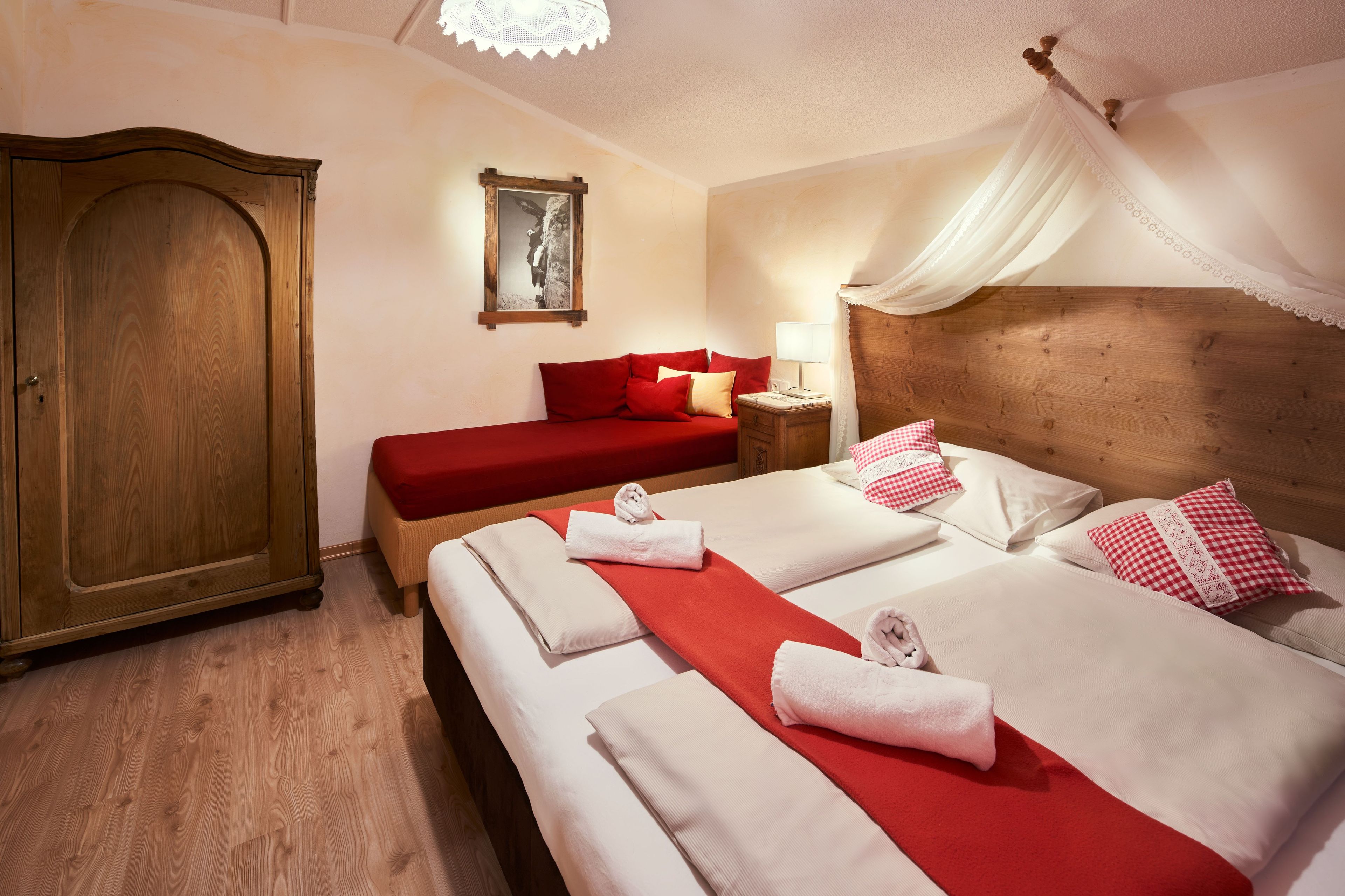 Una camera d'albergo con un'ampia armadiatura in legno, un letto con biancheria rossa e lenzuola bianche, un comodino con una lampada e un letto a baldacchino.
