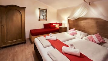 Una camera d'albergo con un'ampia armadiatura in legno, un letto con biancheria rossa e lenzuola bianche, un comodino con una lampada e un letto a baldacchino.