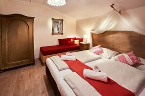 A hotel room with a large wooden wardrobe, a bed with red bedding and white linens, a nightstand with a lamp, and a canopy bed.