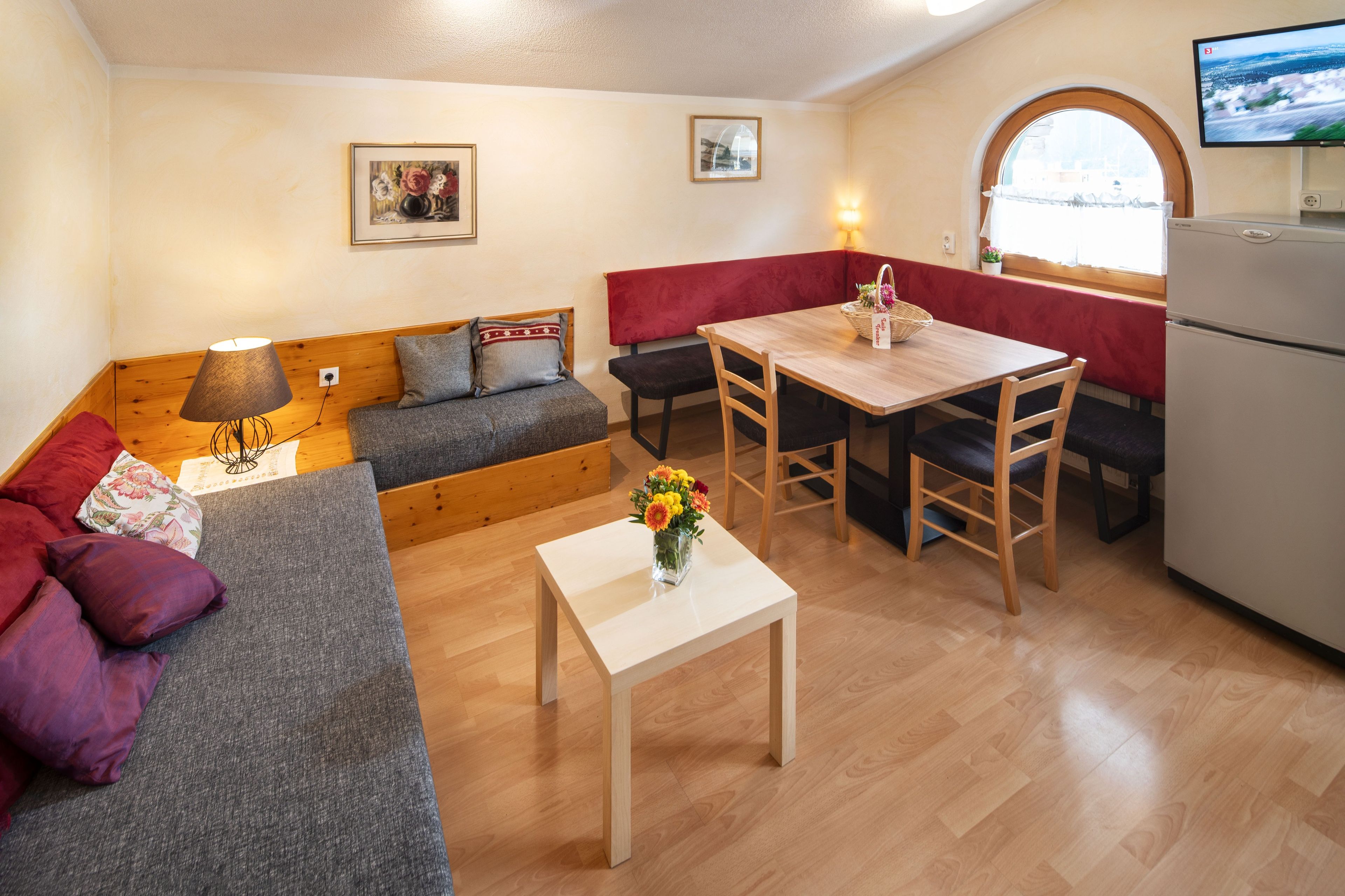 A compact living space with a sofa, a small table with a vase of flowers, a bench, and a dining table with chairs.