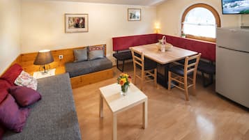 A compact living space with a sofa, a small table with a vase of flowers, a bench, and a dining table with chairs.