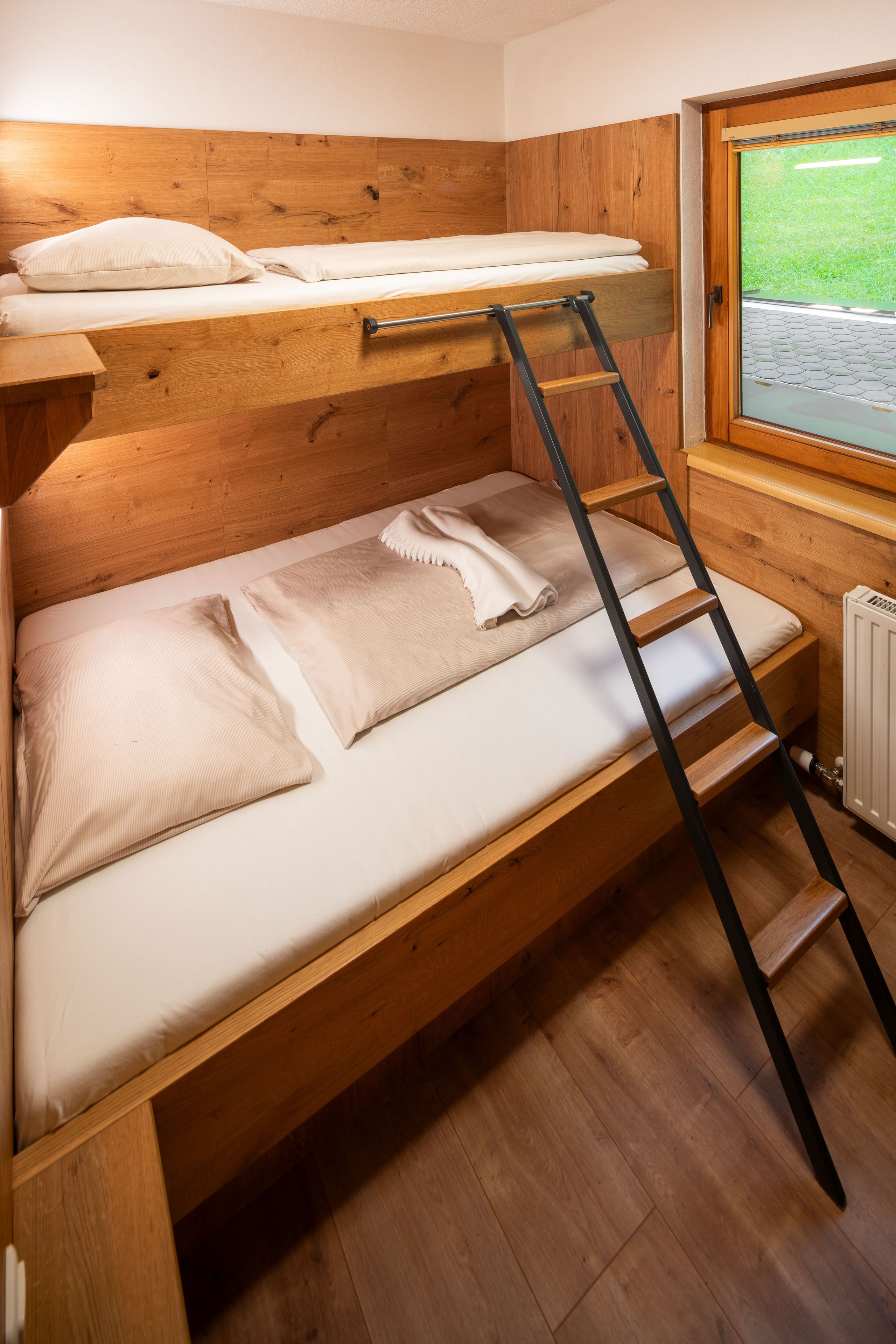 A bunk bed with a ladder, wooden walls, and a window with a view of greenery.