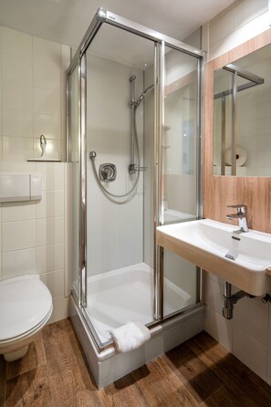 Ein modernes Badezimmer mit einer Duschkabine, einem weißen Waschbecken und einer Toilette.