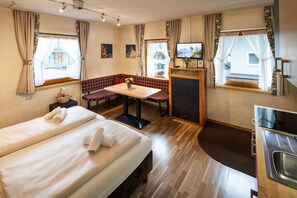 Ein Hotelzimmer mit zwei Betten, einem Esstisch, einer Bank, einem Fernseher und einer Küchenzeile.