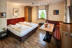 Ein Hotelzimmer mit zwei Betten, einem Esstisch, einer Bank und einem Fenster mit Vorhängen.