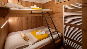 Una cama individual superpuesta con escalera, un radiador blanco y una ventana con cortina.