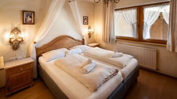 Ein Doppelbett mit weißen Leinen und Handtüchern, ein Holz-Kopfstück, Nachttische mit Lampen, ein Fenster mit Vorhängen und eine Kristallleuchter.