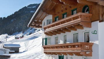 A traditional wooden chalet with a balcony, set against a snowy mountain backdrop.