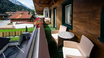 A balcony with wicker furniture, a flower arrangement, and a view of a mountain landscape.