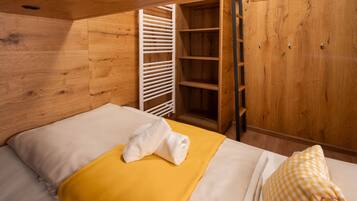 Une pièce en bois avec un lit, une couverture jaune, une serviette blanche, un oreiller à carreaux et une armoire en bois dotée d’une tringle pour suspendre les vêtements.