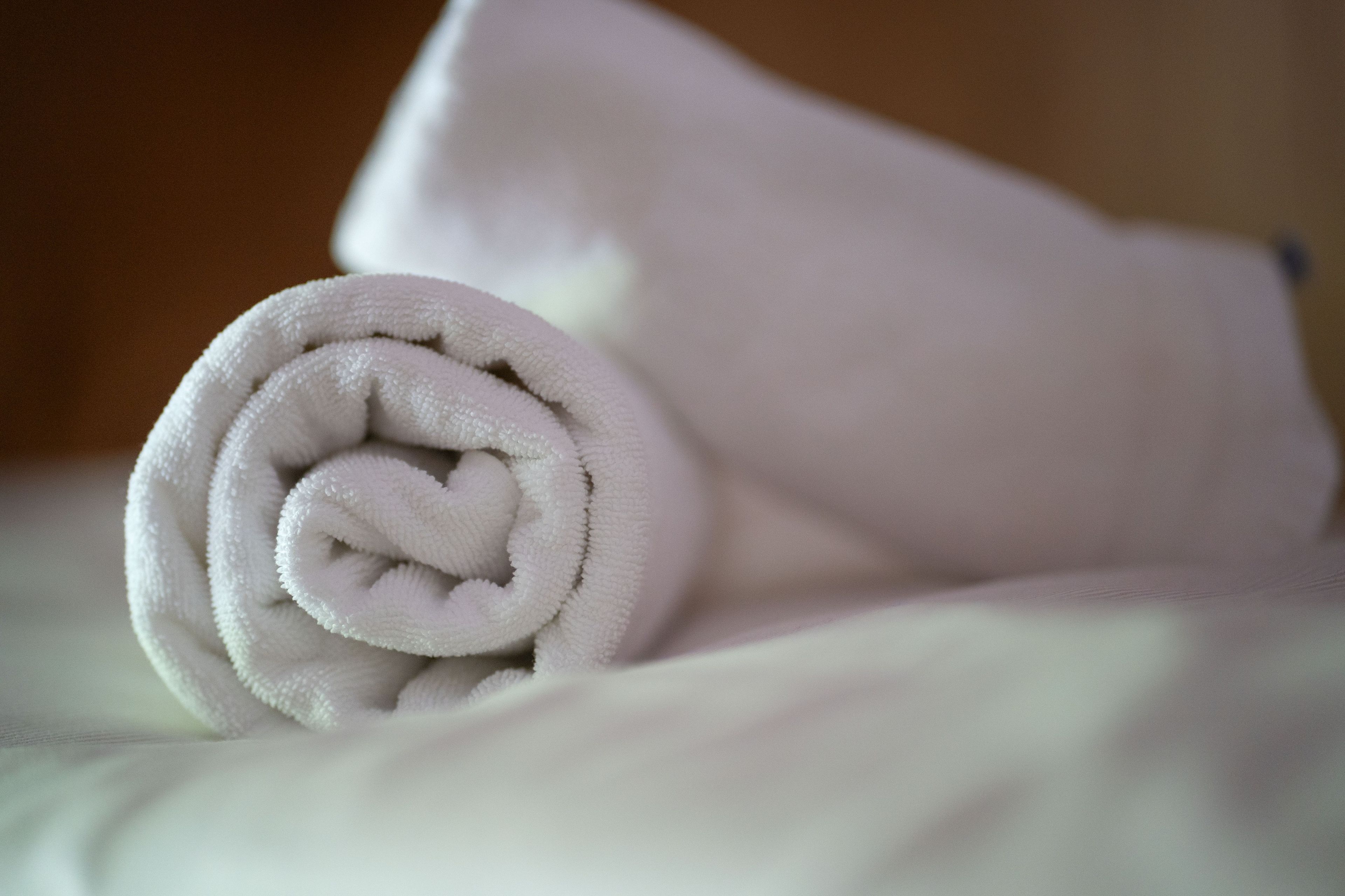 A neatly rolled white towel on a bed.