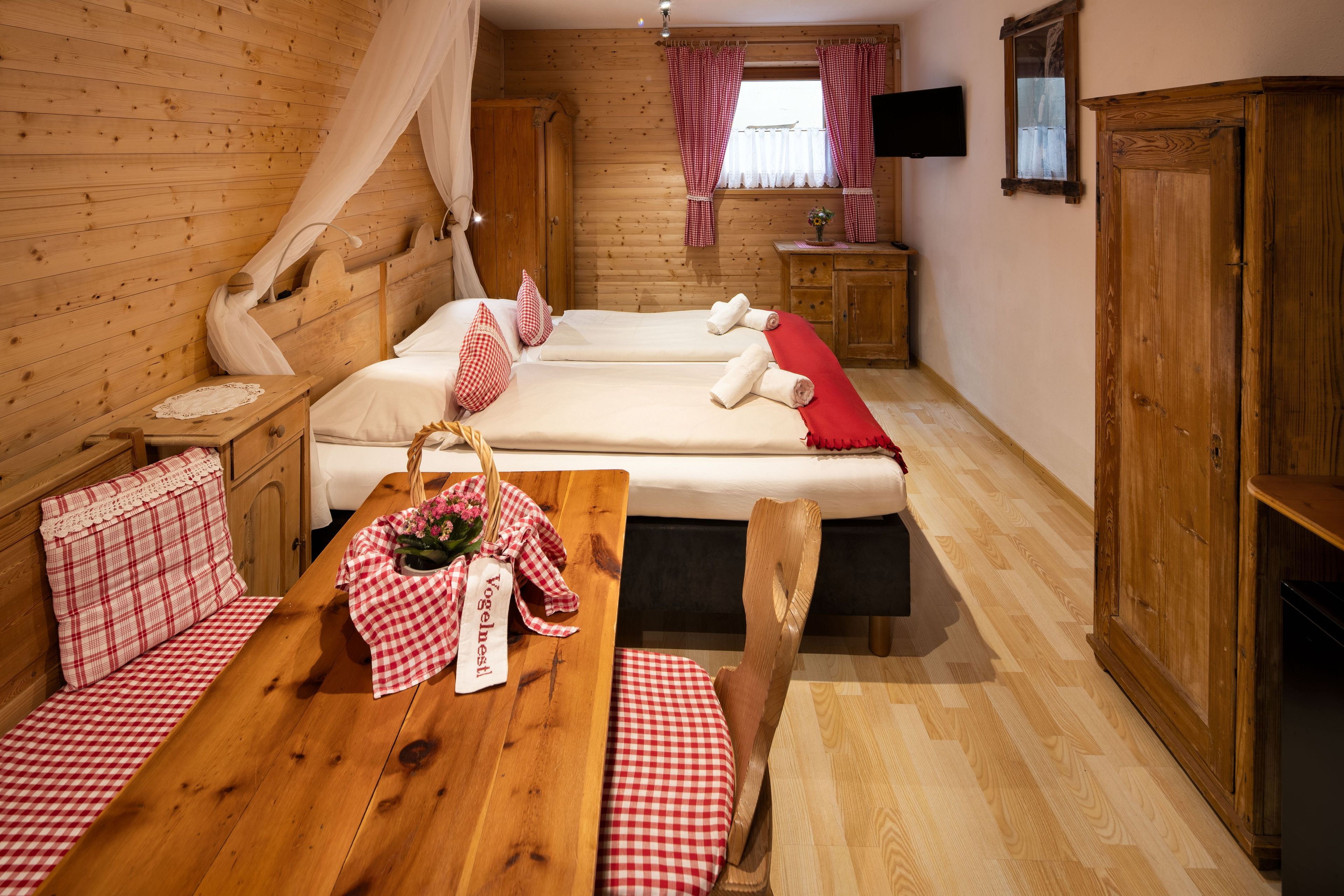 A wooden cabin-style room with two beds, a wooden table with a checkered tablecloth, and a wooden bench.