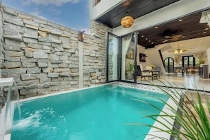 A swimming pool with stone walls, a glass door entrance, and a modern interior with furniture.