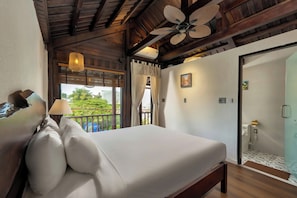 A hotel room with a bed, a ceiling fan, a window with curtains, and a view of greenery outside.