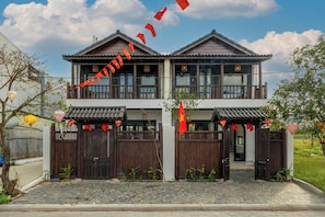 A traditional two-story house with a balcony, wooden gates, and a tiled roof.