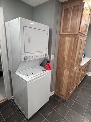 A laundry room with stacked washer and dryer, wooden cabinets, and a tiled floor.