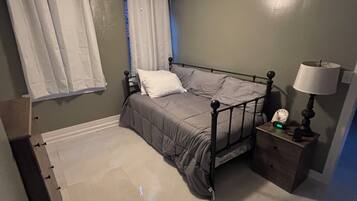 A bedroom with a bed, a nightstand with a lamp, a ceiling fan, and a window with curtains.