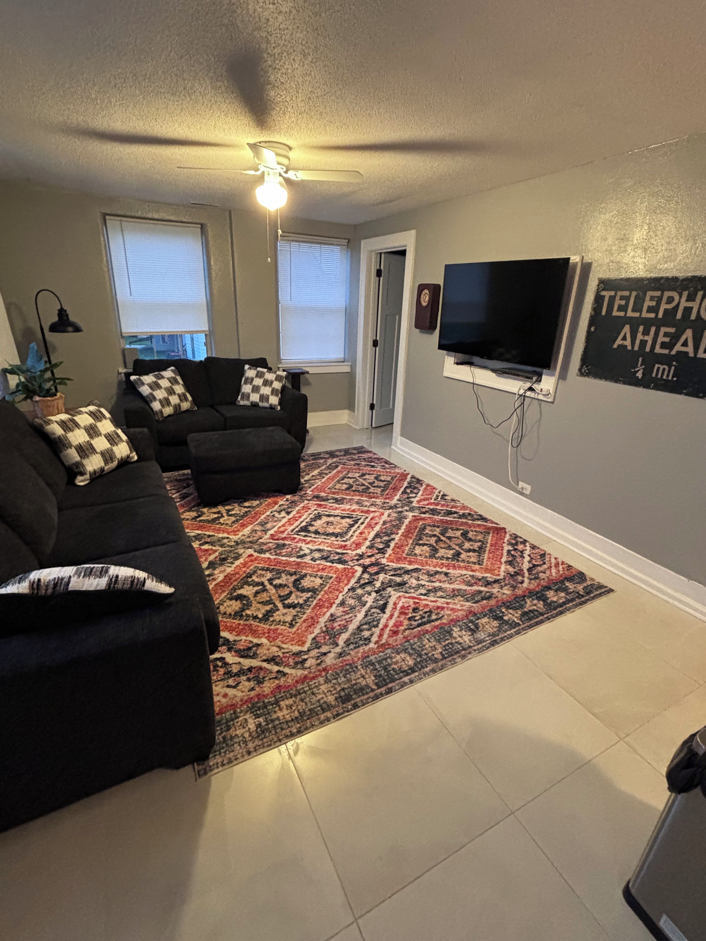 A living room with a black sofa, patterned rug, and a flat-screen TV mounted on the wall.
